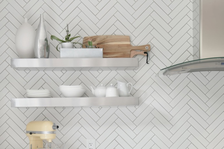 Amsted Bert Argue: A modern kitchen showcases white herringbone tile backsplash, floating silver shelves with white dishes, and a yellow mixer.