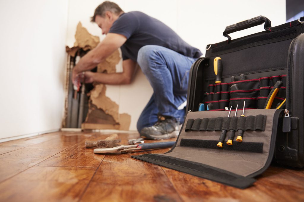 An Amsted employee is engaged in fixing a wall hole with various tools, showcasing professional repair work.